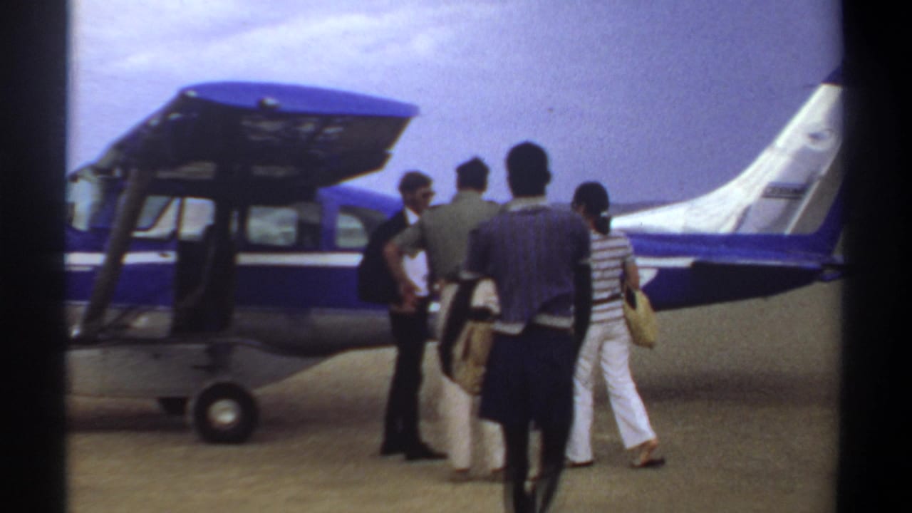 A group stands beside a small blue and white plane with luggage near the open door.
