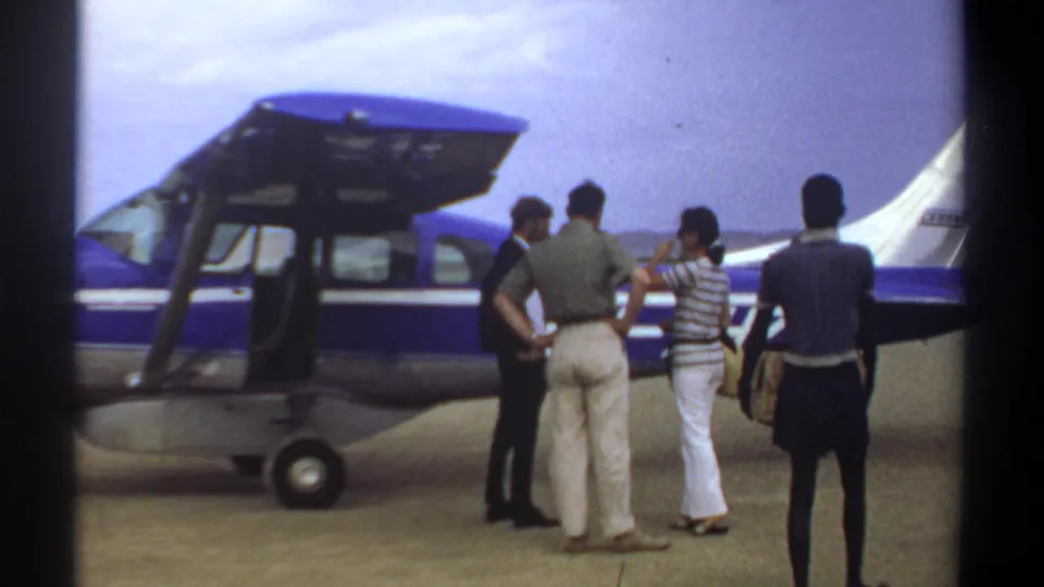 Three travelers stand beside the open door of a small blue and white aircraft in this 1969 Khartoum home-movie frame.
