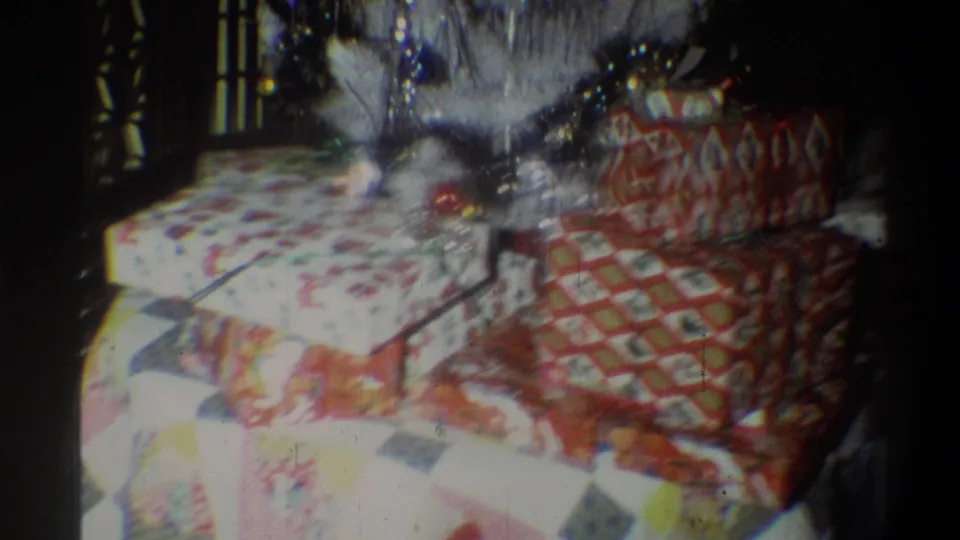 1973 Troy, New York home-movie frame showing wrapped gifts under a white artificial Christmas tree with tinsel and ornaments.