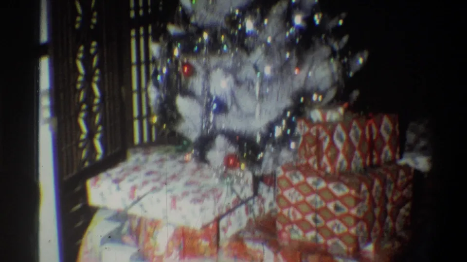 1973 Troy home-movie frame of a white Christmas tree with shiny garland and wrapped presents below it.