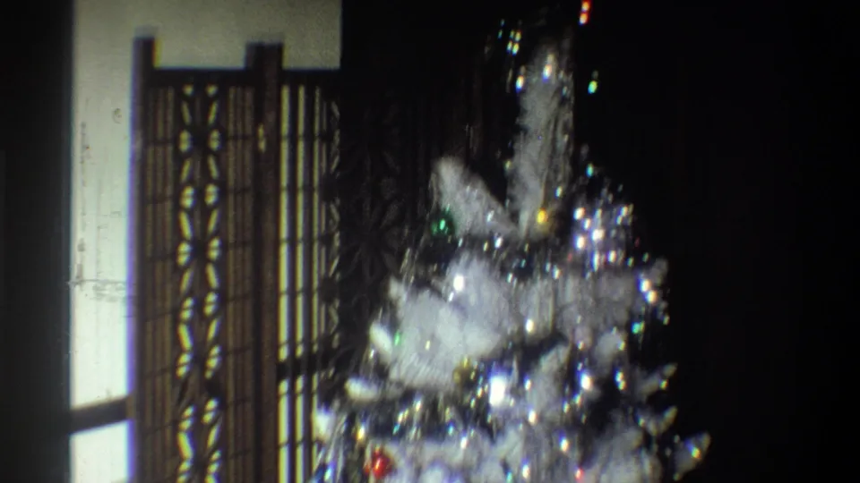 A white artificial Christmas tree with tinsel and colored ornaments appears in a dark 1973 Troy holiday interior.