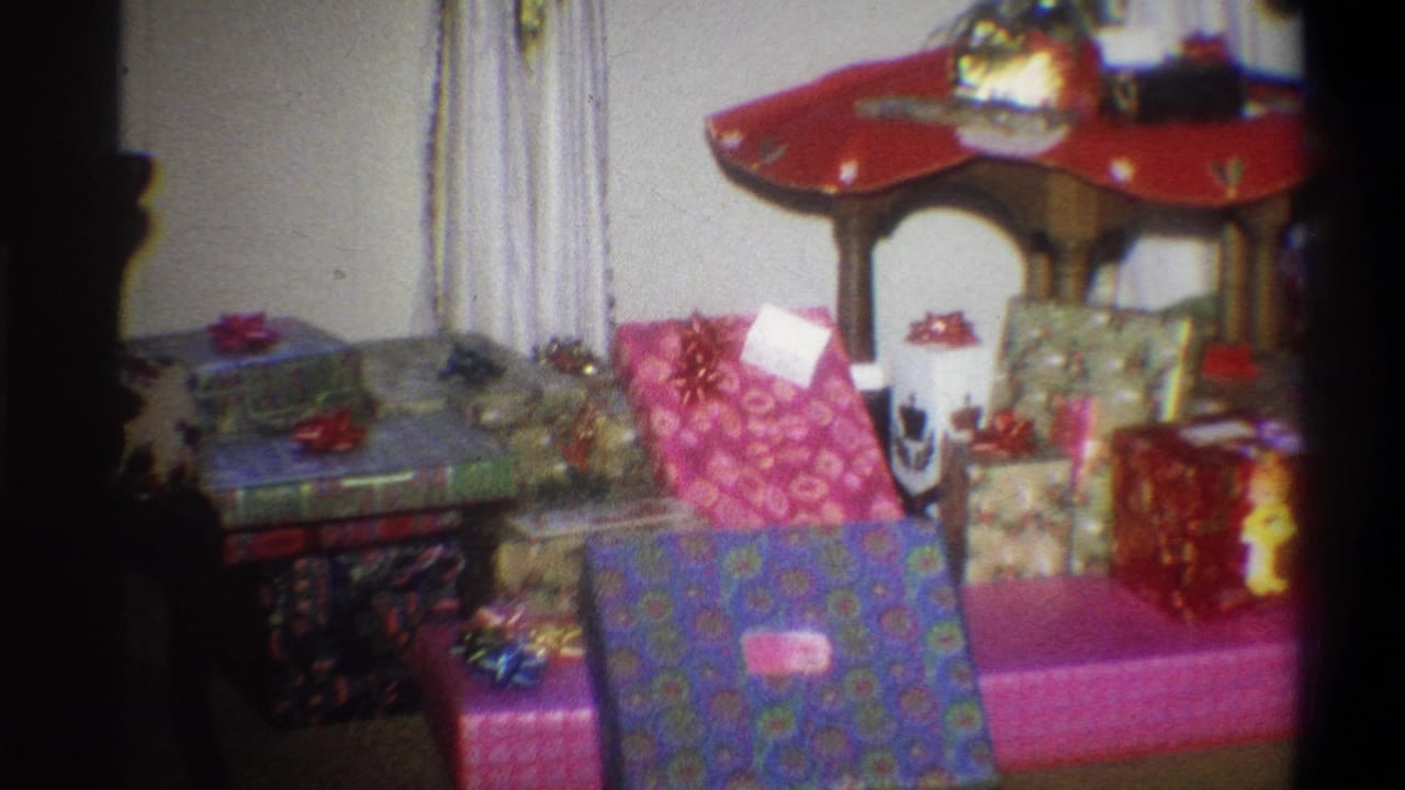 Pile of wrapped presents with bows in front of a red-topped table.