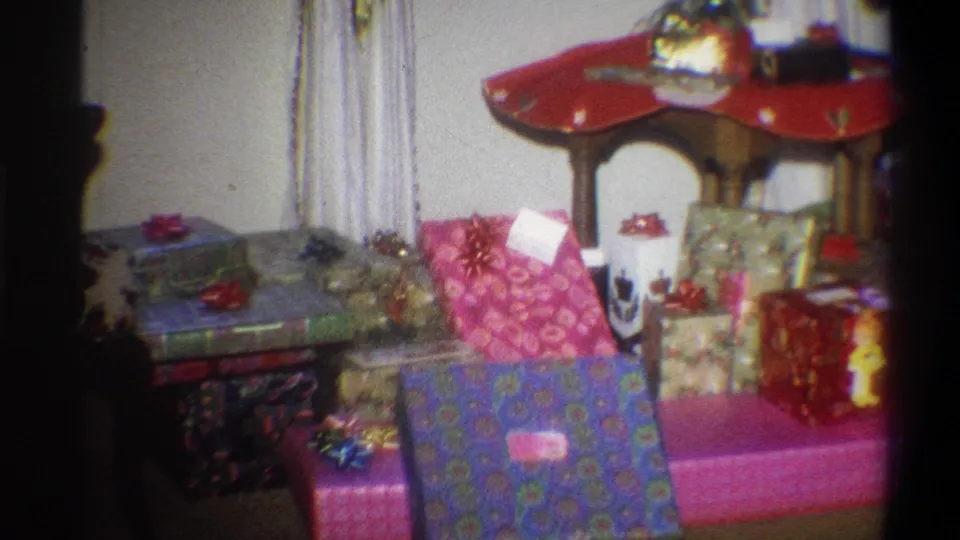 1973 Troy, New York frame showing pink, purple, green, and red wrapped gifts arranged in a holiday home interior.