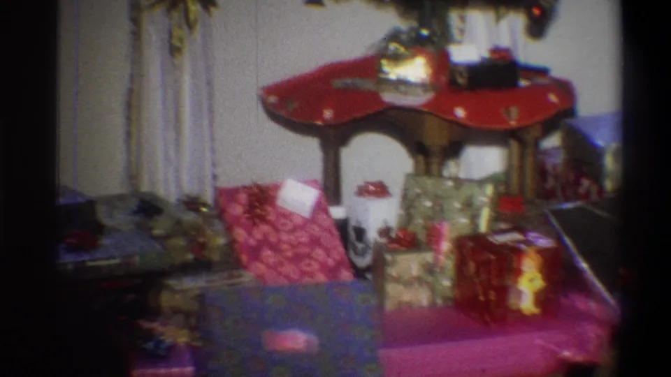 1973 Troy, New York home-movie frame with wrapped presents, shiny bows, curtains, and holiday decorations in soft 8mm focus.
