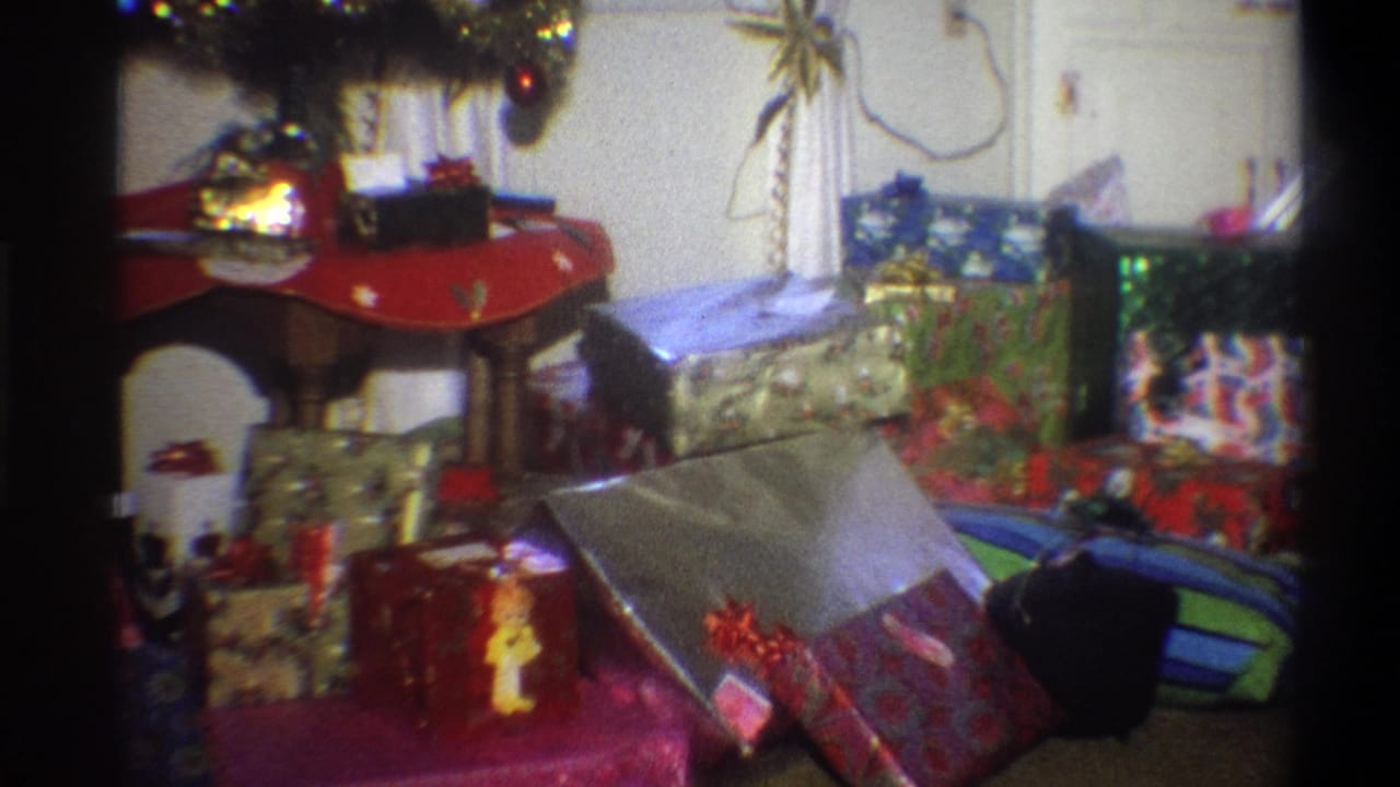 Christmas presents arranged under a lit tree in a living room.