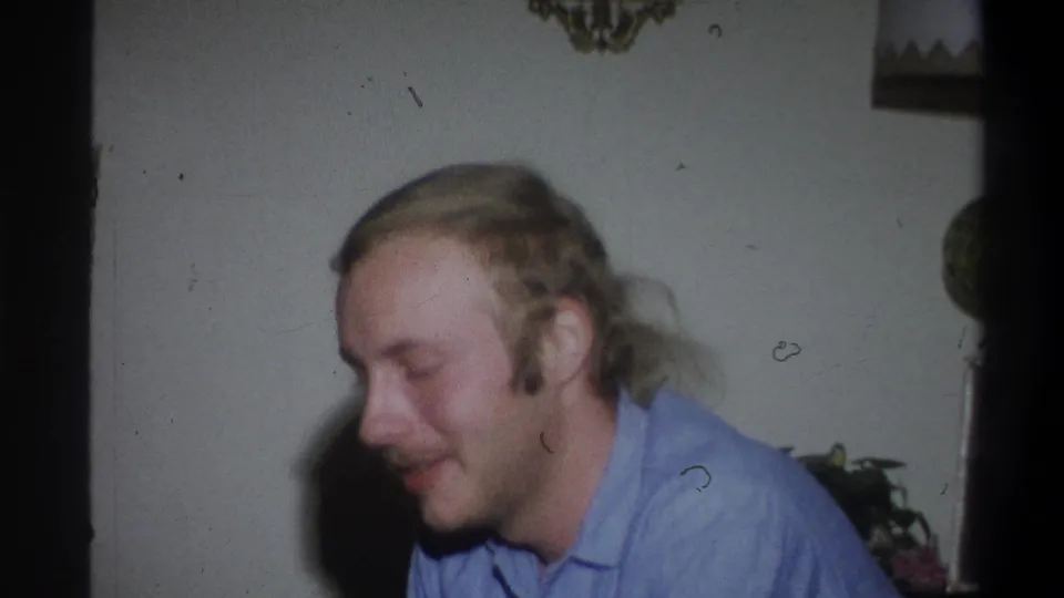The young man appears in profile or three-quarter view, looking down in a private interior during the 1973 Troy home movie.