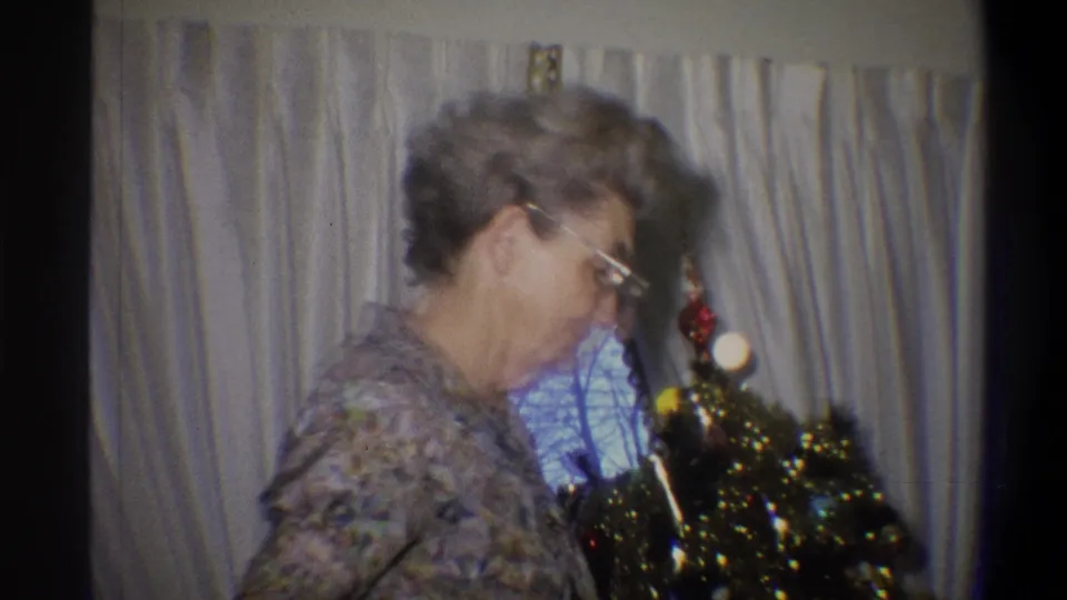 1973 Troy, New York frame showing the woman turning beside the decorated tree, with curtains and window behind her.