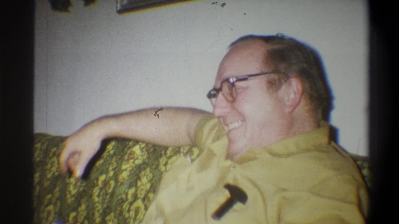 Man in glasses laughing while reclining on a floral couch.