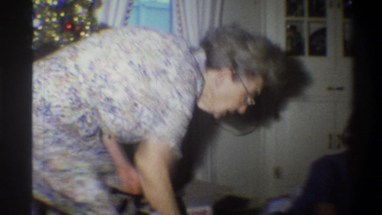 An older woman in a patterned dress bends near a lit Christmas tree inside a Troy, New York home in 1973.
