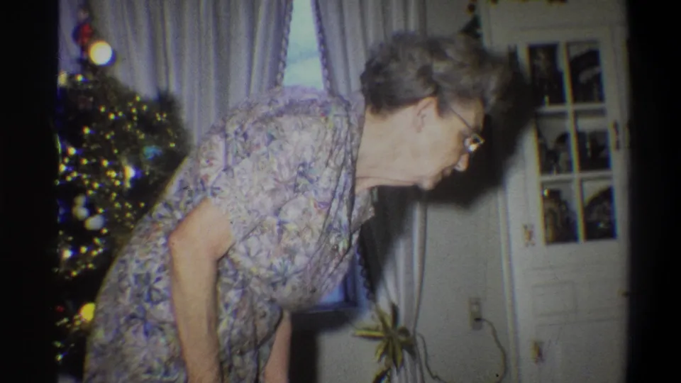 In the final frame, the older woman leans forward near the Christmas tree as glass-paneled doors and a houseplant appear behind her.