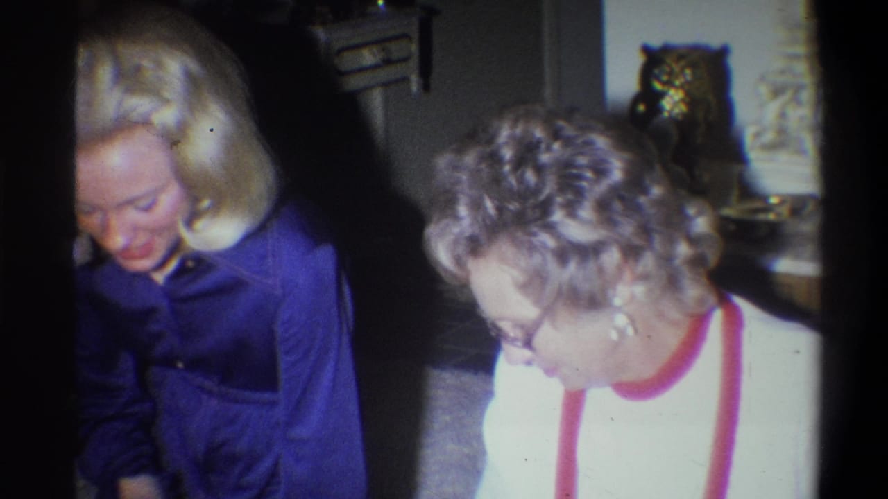 Two adult women in a Troy, New York living room look downward near a fireplace surround and owl figurine in 1973 home-movie footage.