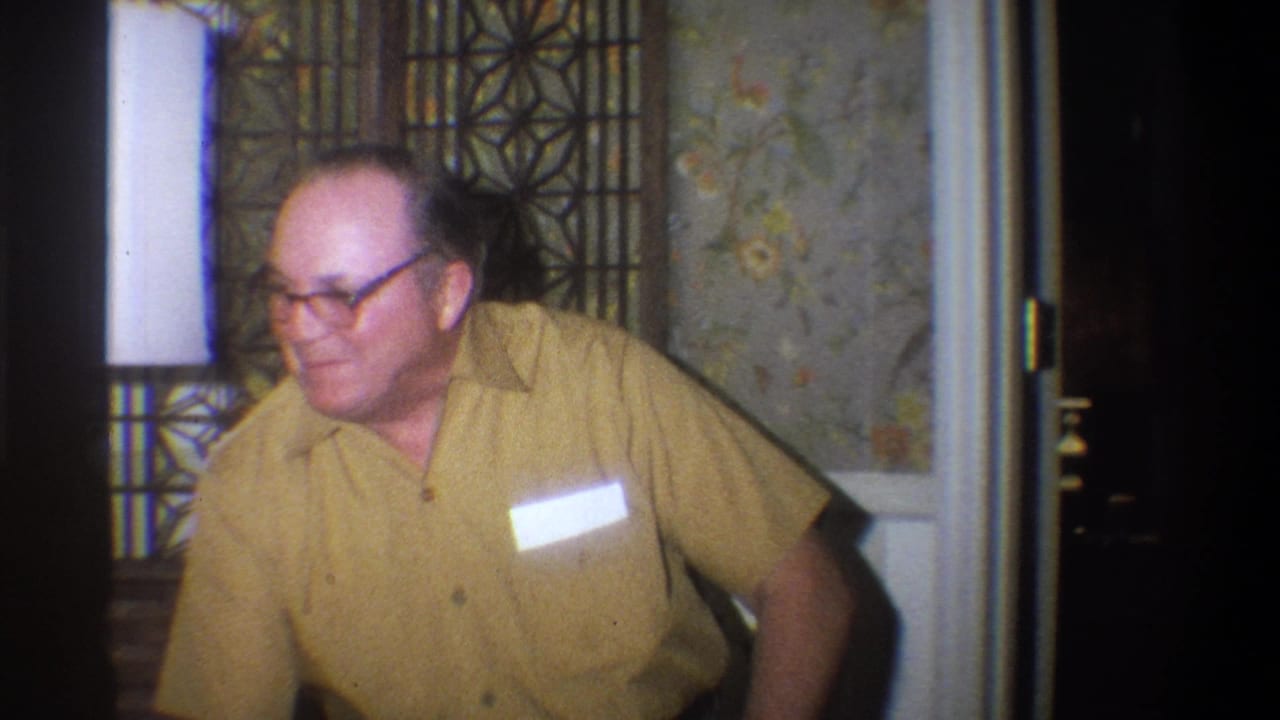 Man with glasses in a yellow shirt seated in a decorated room.