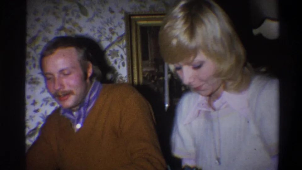 The seated man and woman look downward together in a warm 1970s private-room setting in Troy, New York.
