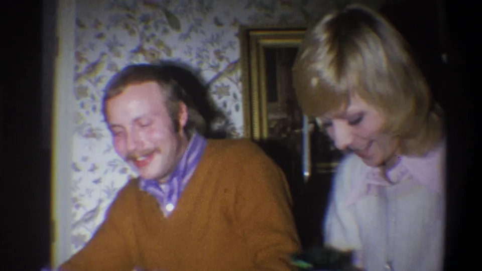 A mustached man smiles beside a blonde woman in light clothing during 1973 home-movie footage from Troy, New York.