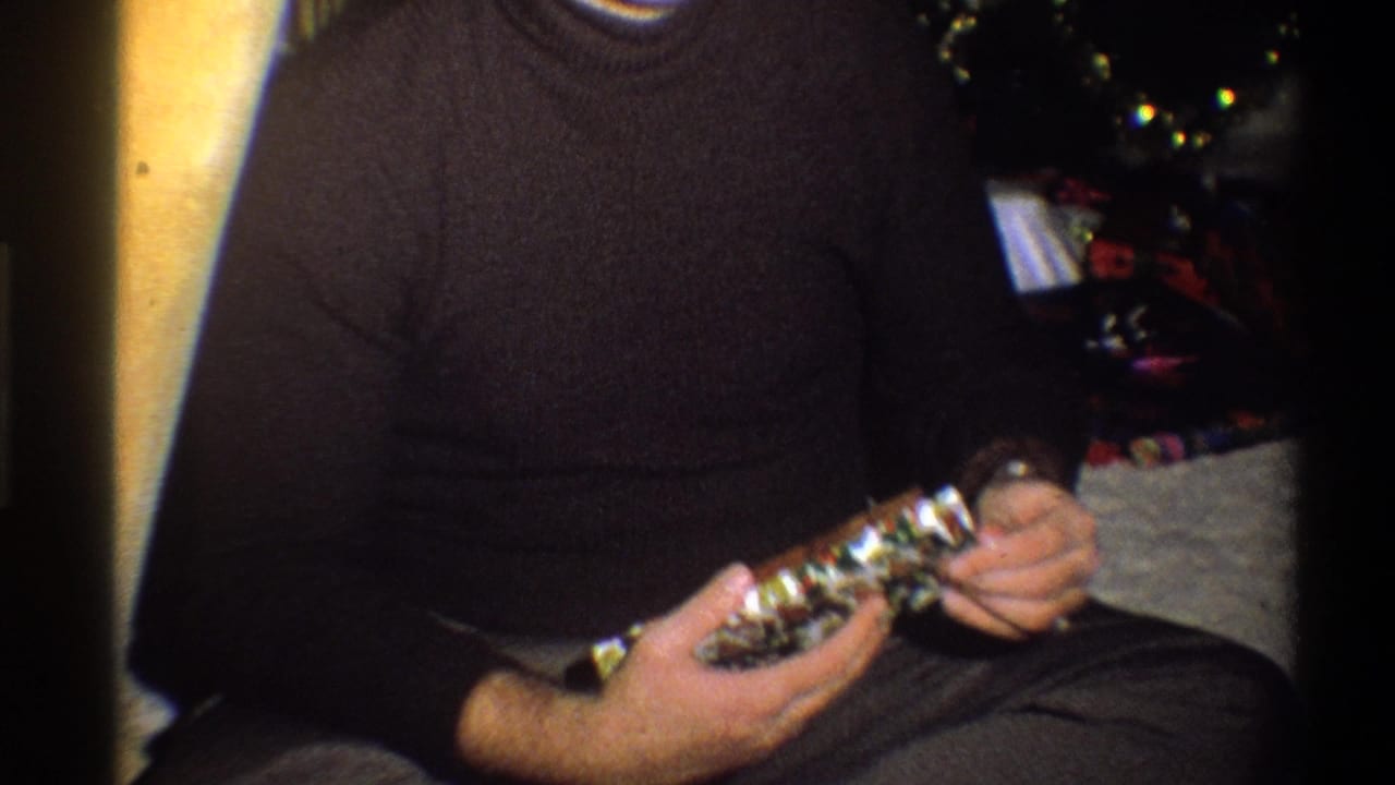 1973 Troy, New York home-movie frame of a seated man holding a gift beside a decorated Christmas tree.