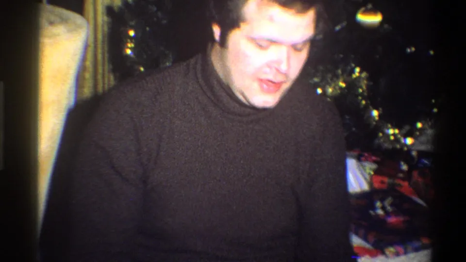 1973 Troy, New York home-movie frame of the man looking down near the Christmas tree and presents.