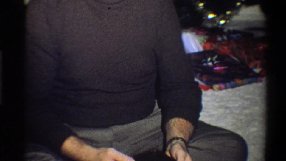 1973 Troy, New York home-movie frame with a cropped seated man, holiday gifts, and part of the tree.