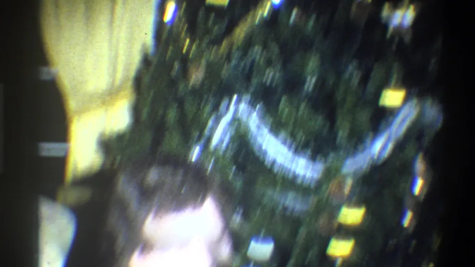 Soft, handheld 1973 Troy, New York frame showing a blurred man near a Christmas tree with tinsel and ornaments.