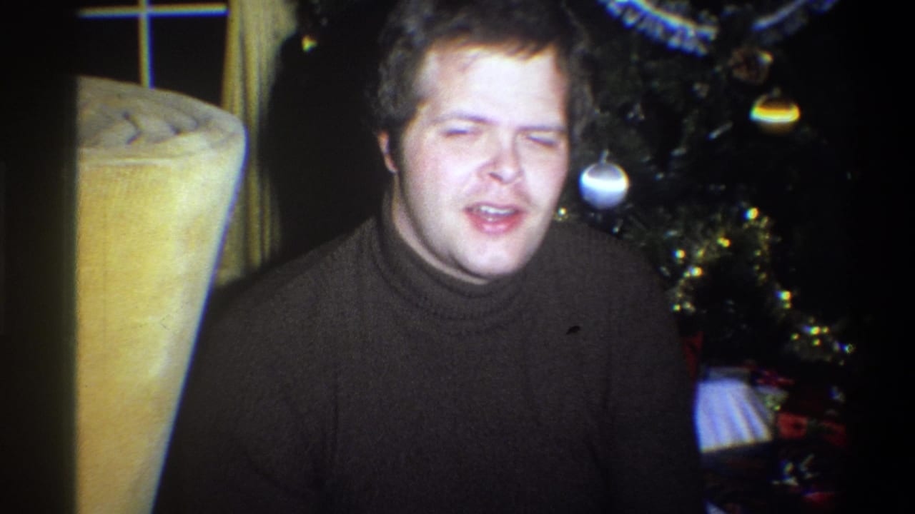 Young man in a dark turtleneck smiles beside a decorated Christmas tree in a 1973 Troy, New York home interior.