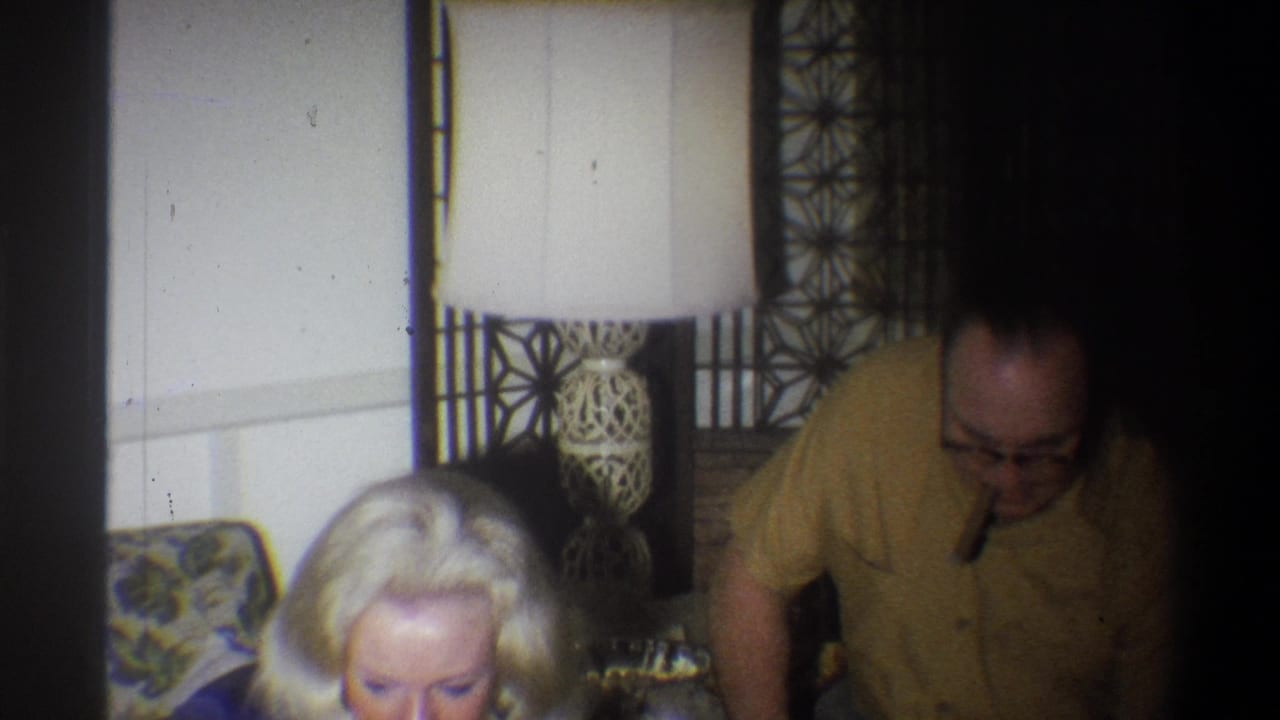 Blonde child and seated man near a floral couch in a dim living room.