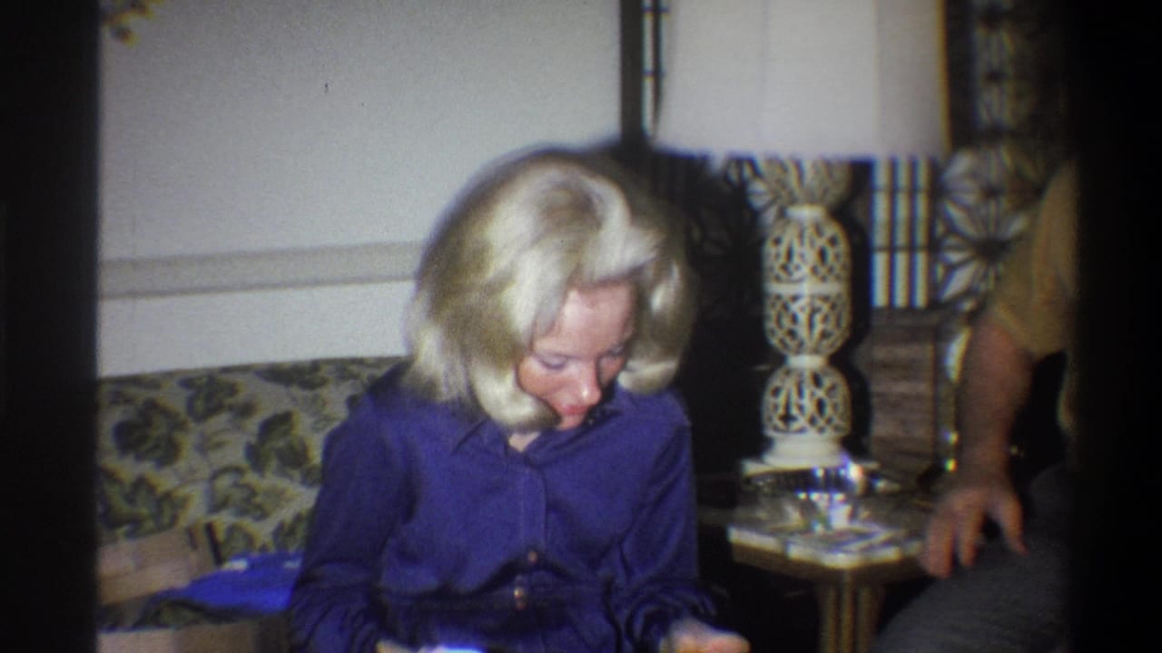 Woman seated on couch while a man in a yellow shirt stands partly in frame.