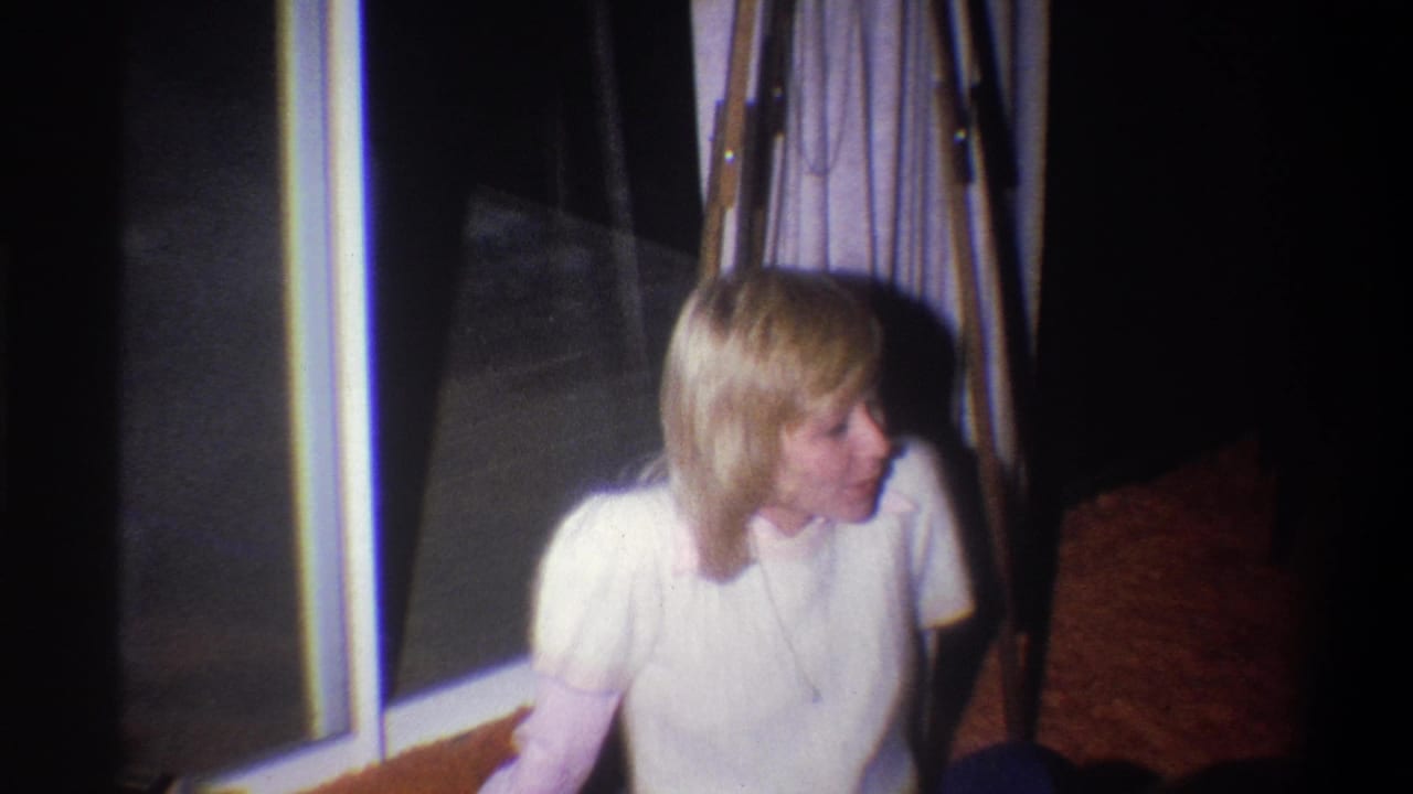 The blonde woman remains seated near the window, looking off-frame in a softly exposed 1973 Troy living-room scene.