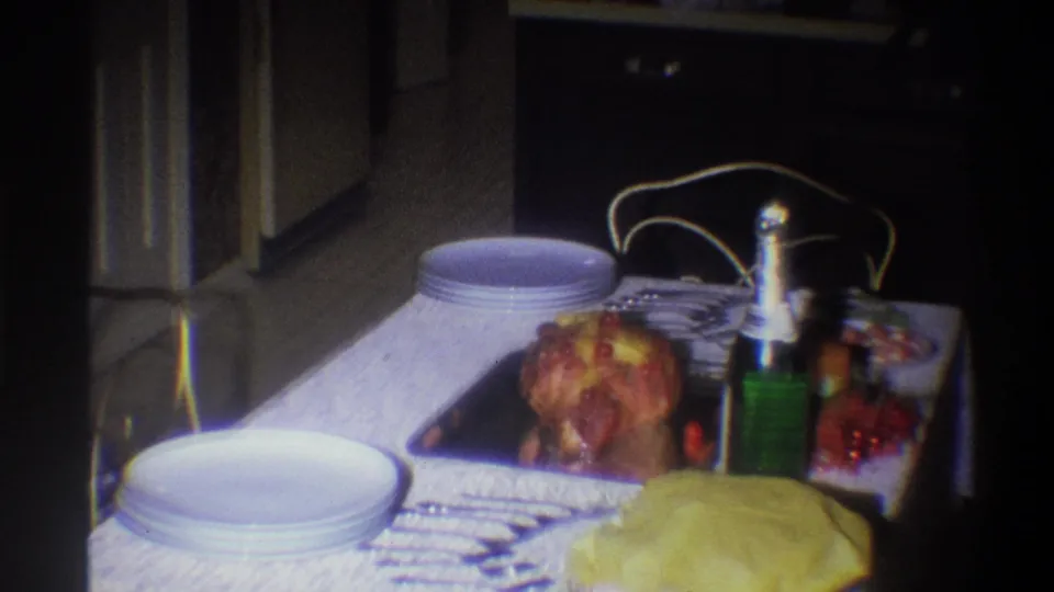 A repeated view of the Troy home dinner table shows roast chicken, white plates, a green bottle, and serving dishes in soft 8mm light.