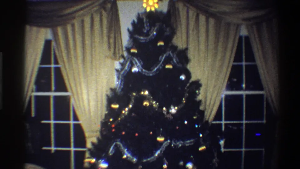 1973 Troy, New York home-movie view of the decorated Christmas tree, with tinsel, ornaments, small lights, and cream drapes behind it.