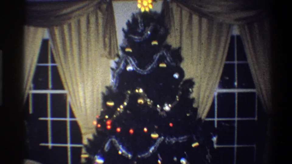 1973 Troy, New York frame showing the Christmas tree with red and warm lights, silver garlands, ornaments, cream drapes, and window panes.