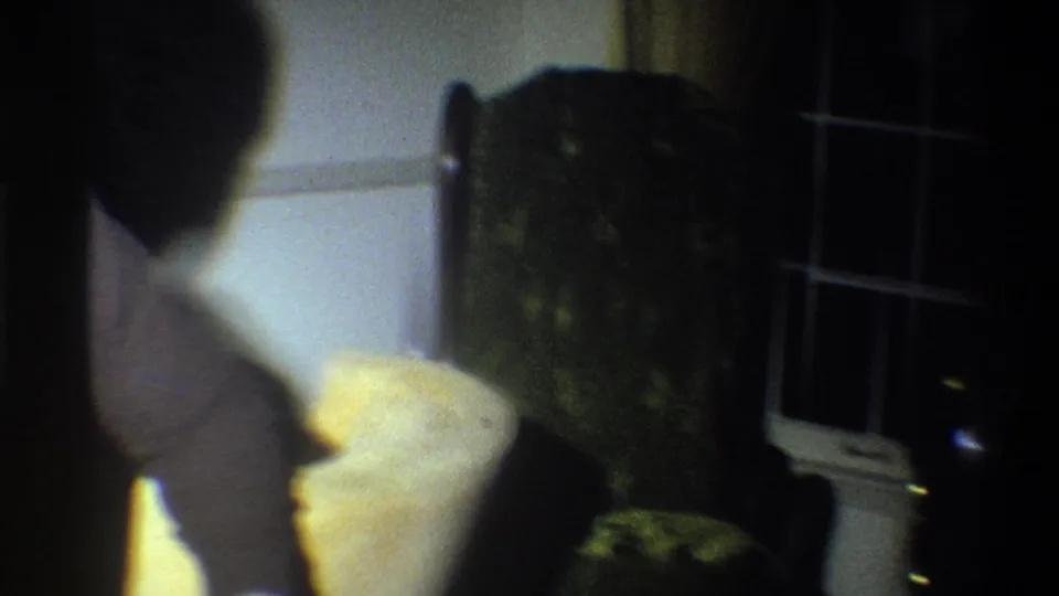 An adult in a light sweater turns near a window and Christmas tree in the Troy, New York holiday interior.