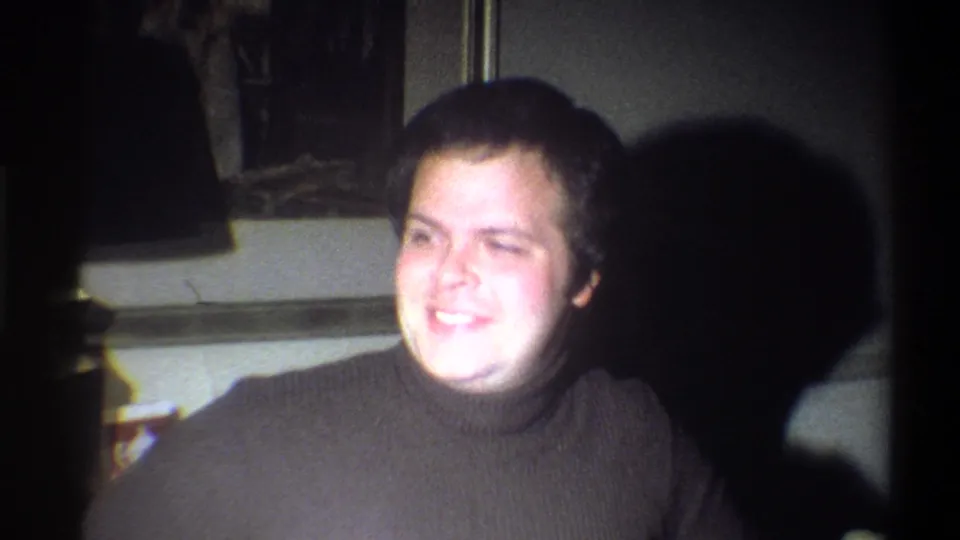 Young man in a brown turtleneck smiles toward the camera inside a Troy, New York home interior in 1973.