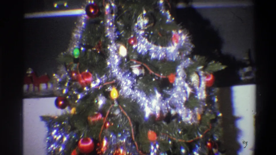 1973 Troy, New York 8mm frame showing the upper portion of a decorated indoor Christmas tree with silver tinsel, red baubles, and glowing colored lights.