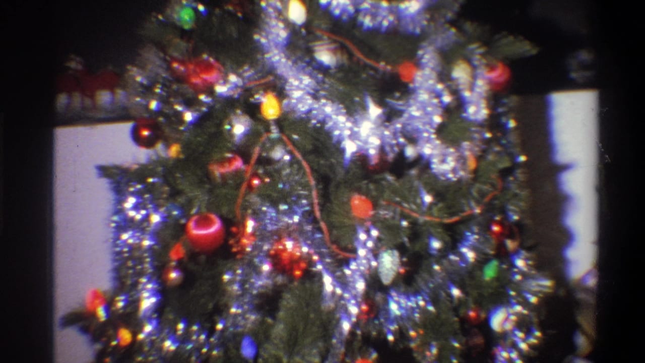 1973 Troy, New York 8mm frame showing a close scan across a decorated Christmas tree with reflective tinsel, red ornaments, and multicolored lights.