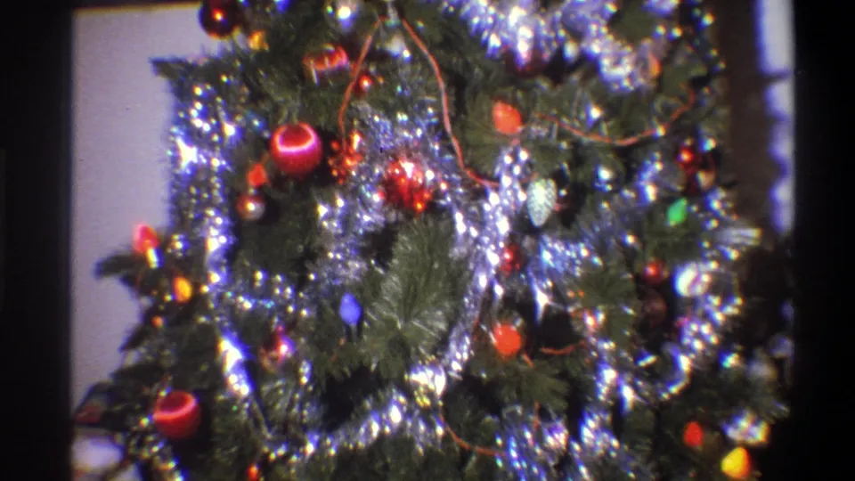 1973 Troy, New York 8mm frame showing the lower part of a decorated indoor Christmas tree with silver garland, red ornaments, colored lights, and partial presents below.