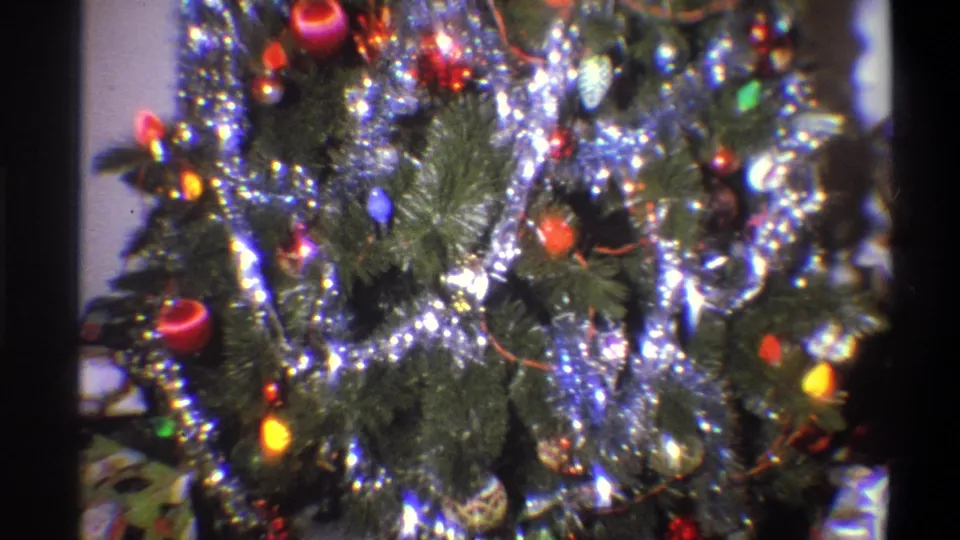 1973 Troy, New York 8mm frame showing a dense section of the indoor Christmas tree with reflective tinsel, red ornaments, green branches, and glowing colored bulbs.