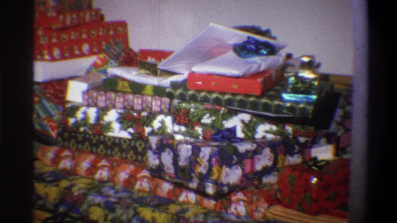 1973 Troy, New York 8mm frame showing a dense pile of wrapped Christmas presents with holiday-patterned paper and bows in a home interior.
