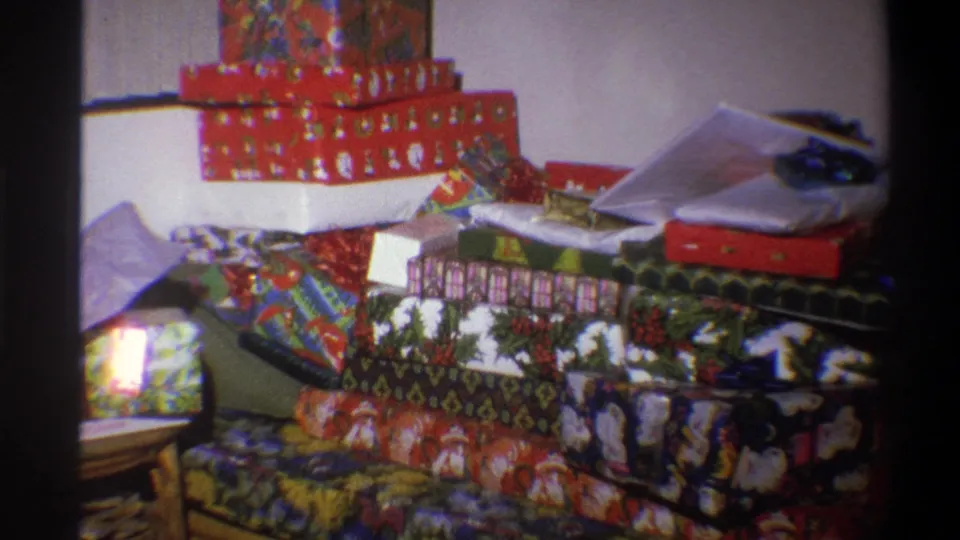 1973 Troy, New York 8mm frame of wrapped Christmas presents piled in a domestic room, including red holiday boxes and patterned paper.