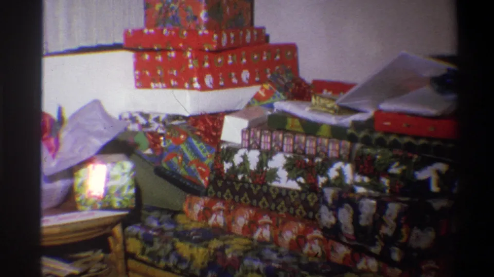 A 1973 Troy, New York home-movie frame shows Christmas gifts piled on the floor, with red boxes and mixed holiday wrapping visible.