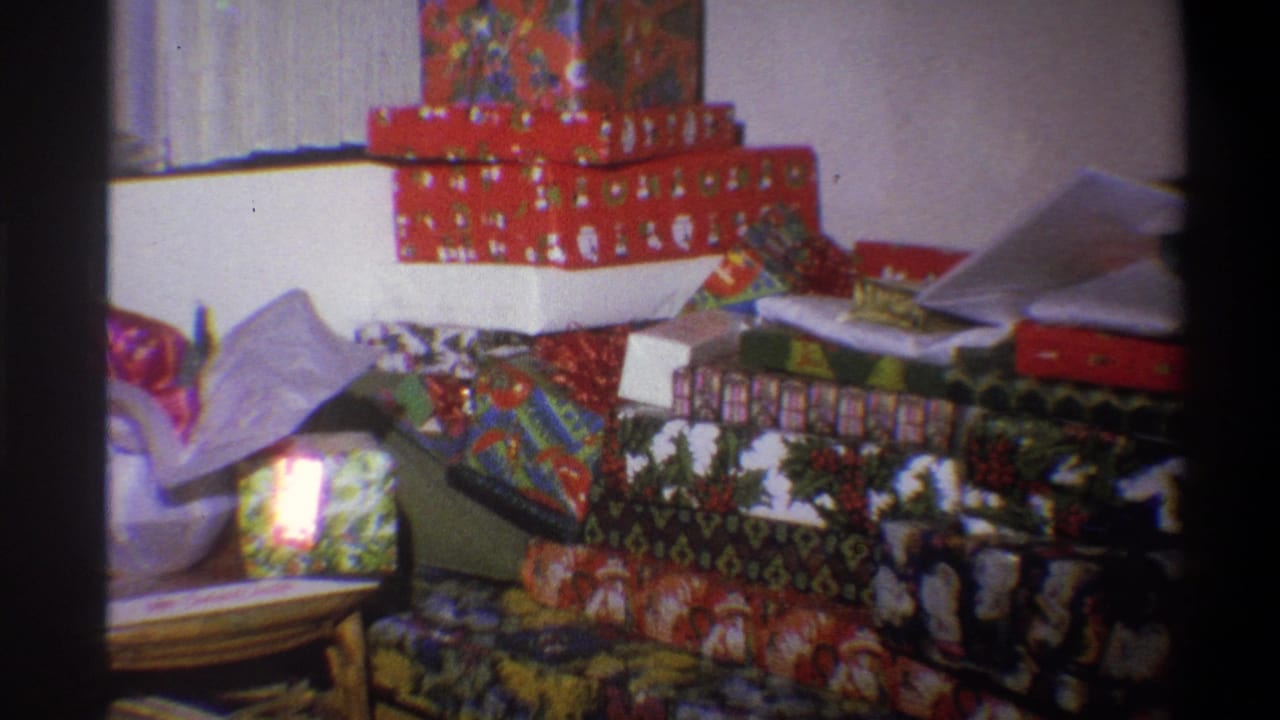 1973 Troy, New York home-movie frame showing a large pile of wrapped Christmas presents arranged in a living room.