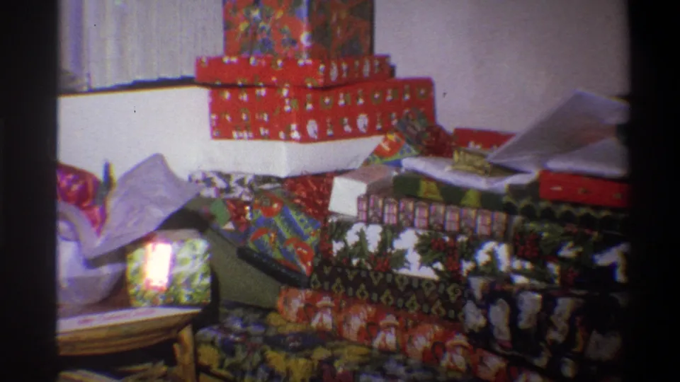 1973 Troy, New York home-movie frame showing a large pile of wrapped Christmas presents arranged in a living room.