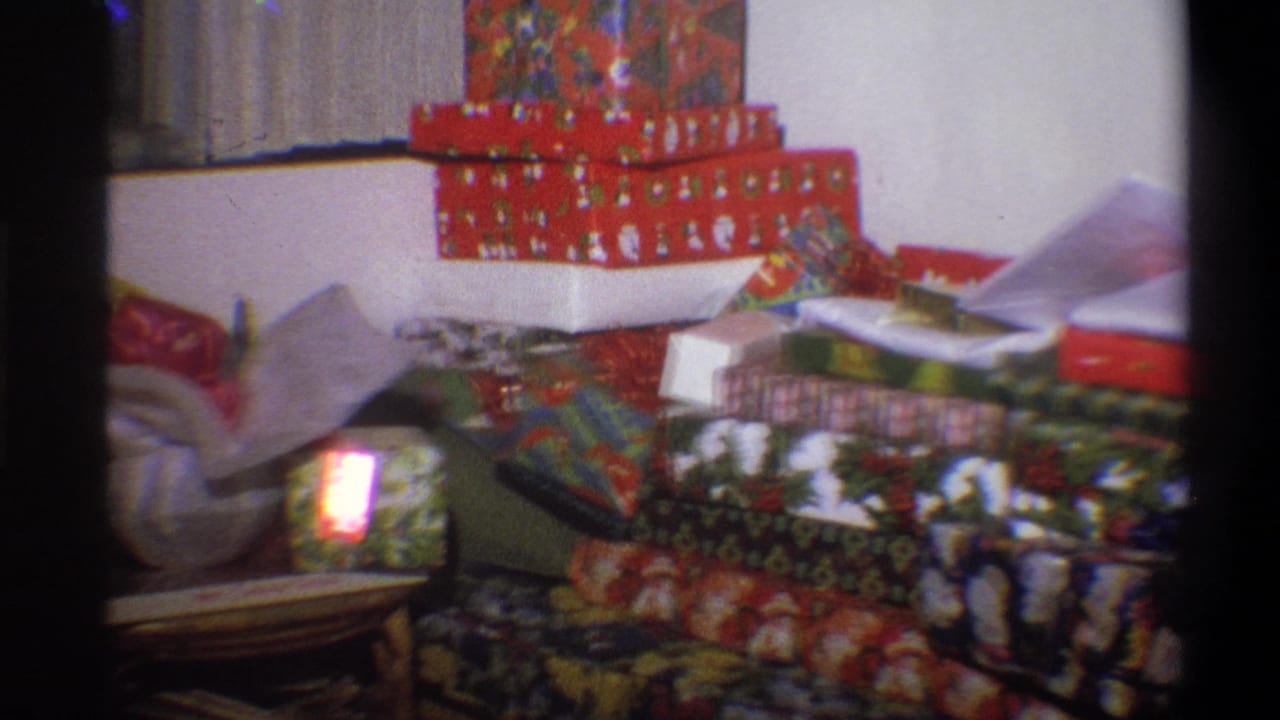 1973 Troy, New York frame with holiday gifts piled in a living room, including a small bright glow on a wrapped box.