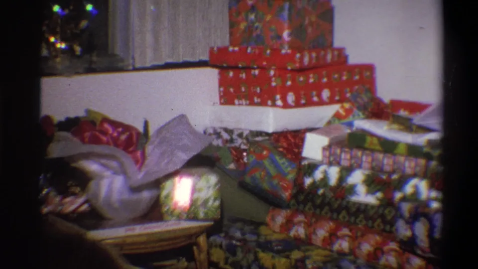 1973 Troy, New York frame showing a living-room pile of wrapped Christmas gifts, viewed in soft 8mm color.