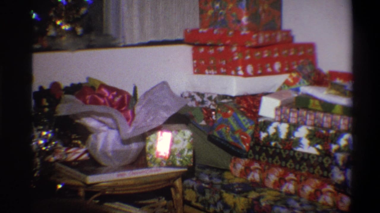 1973 Troy, New York 8mm frame showing wrapped Christmas presents, tinsel, tree lights, and a small table inside a family home.