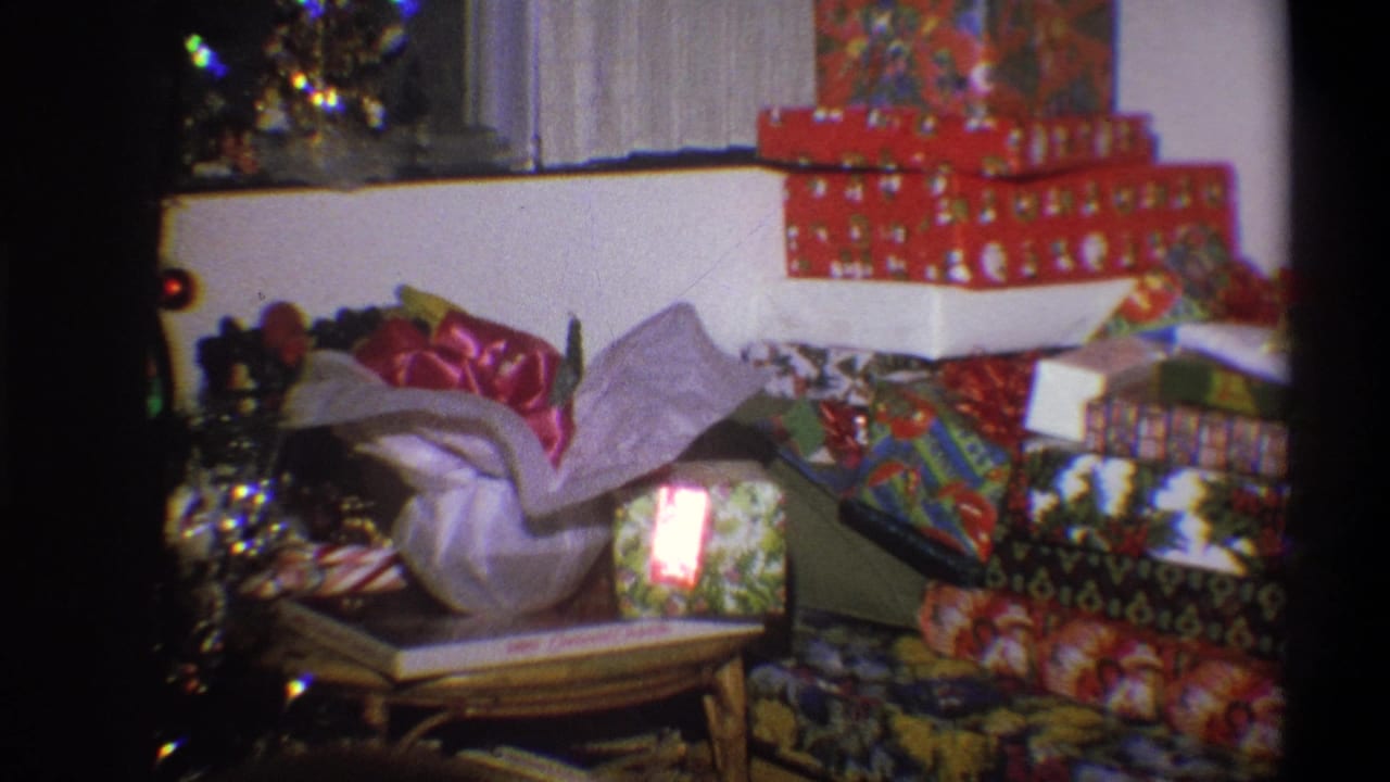 A Troy, New York home-movie frame from 1973 shows layered Christmas gifts, patterned wrapping, tinsel, and soft 8mm color indoors.