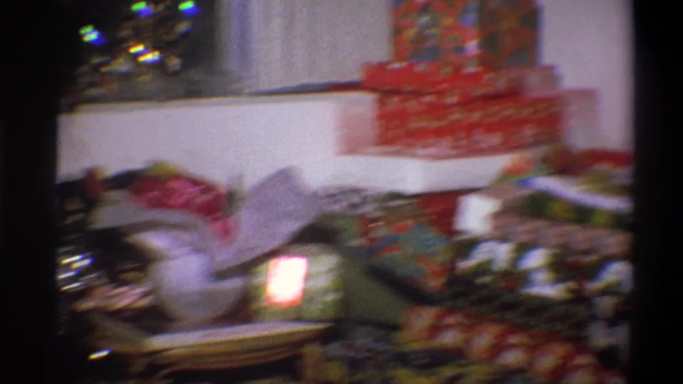 Motion-blurred 8mm frame of Christmas presents, red patterned boxes, tinsel, and domestic furnishings in the Troy holiday interior.