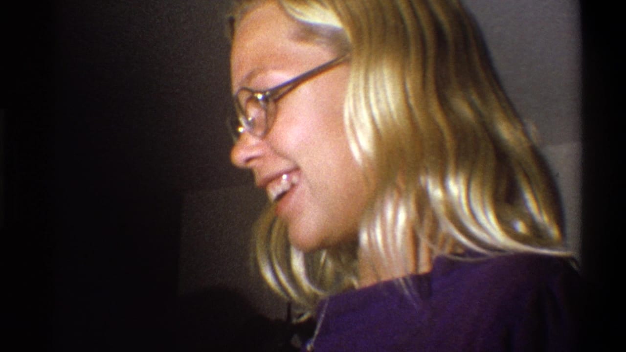 In 1973 Troy, New York home-movie footage, a blonde woman in glasses and a purple top smiles in close profile indoors.