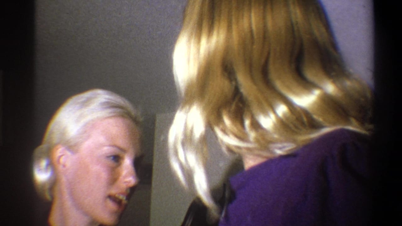Two blonde women appear in a close indoor 1973 Troy home-movie frame, one facing the camera area and one turned away.