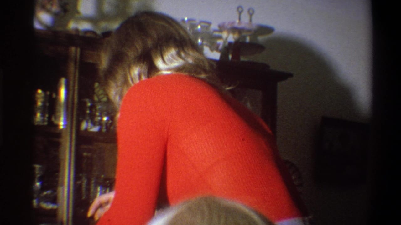 Woman in a red shirt bends near a wooden china cabinet in a dim interior.