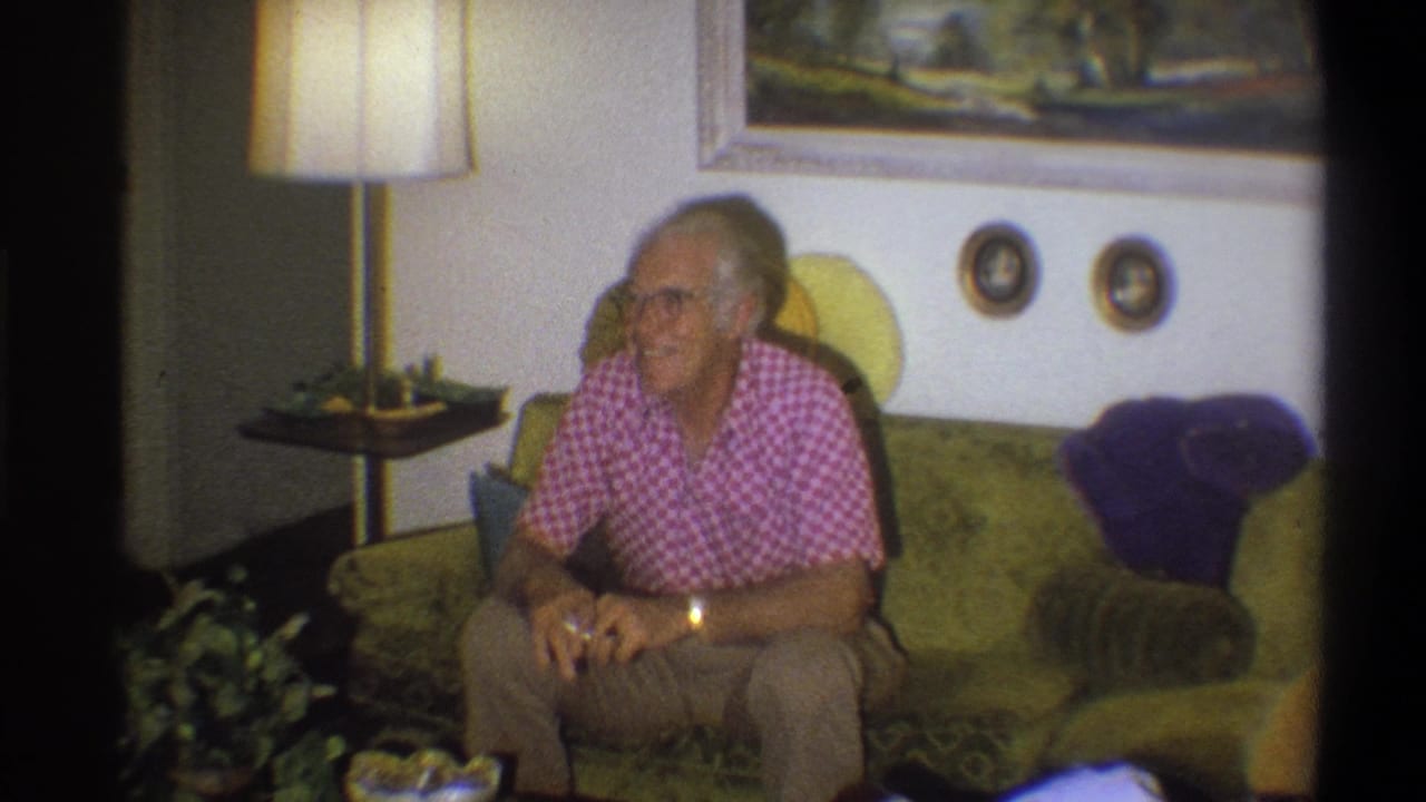 In 1973 Troy, New York home-movie footage, an elderly man in a pink checkered shirt sits on a green couch near a lamp and wall art.