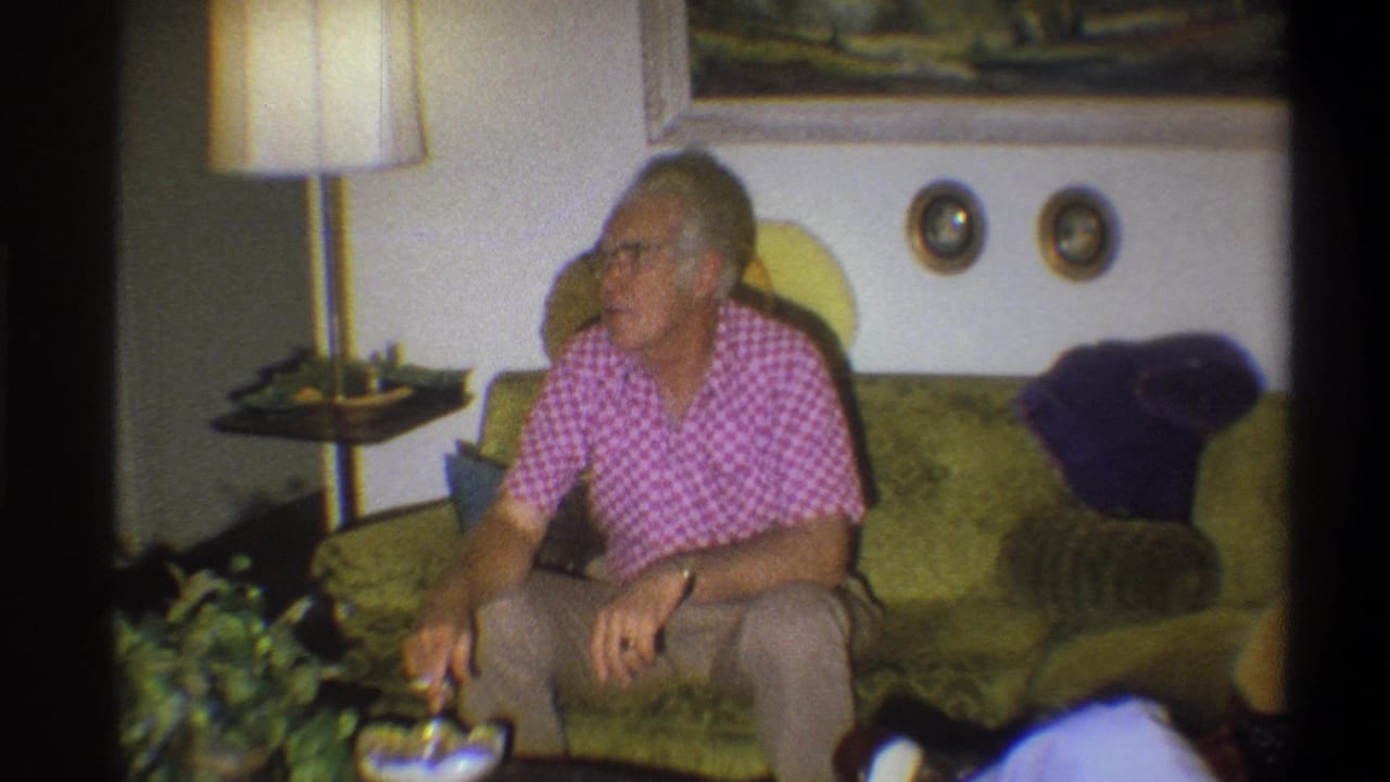 The elderly man remains seated on the green couch, turned toward the side of the room in the Troy, New York living-room scene.